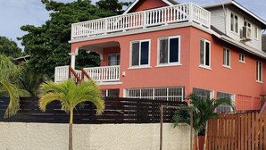 Ein zweistöckiges Haus mit Balkon, umzäunter Garten und Palmen.