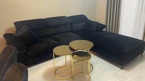 Un canapé noir modulable, avec trois petites tables rondes dorées devant.