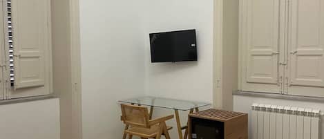 Habitación de hotel con cama, escritorio, silla, televisor y radiador.