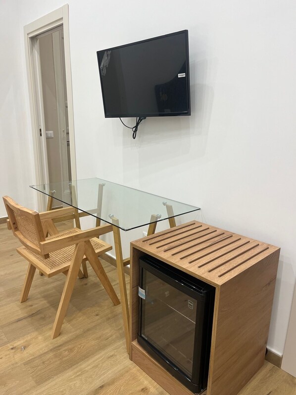 A room with a glass-top table, two wooden chairs, a television mounted on the wall, and a small wooden cabinet with a glass door. - In the heart of Palermo, just a minute from Mondello, nestled in the neighborhood (Palermo)