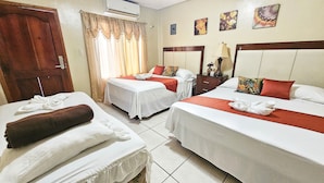 Habitación de hotel con dos camas, una puerta de madera, una ventana con cortinas, una mesita de noche, una lámpara y decoración en la pared.