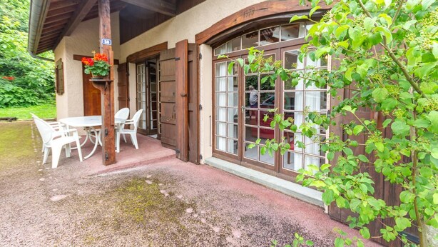 A rustic building with a covered patio, a table with chairs, and a large window with a view of greenery. - LEGENT - GRESY SUR AIX (GRESY SUR AIX)