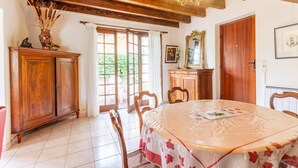 A dining area with a round table covered in a floral tablecloth, wooden chairs, a cabinet, and a chandelier. - LEGENT - GRESY SUR AIX (GRESY SUR AIX)