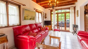 A spacious living room with a red leather sofa, a wooden coffee table, and a chandelier. - LEGENT - GRESY SUR AIX (GRESY SUR AIX)
