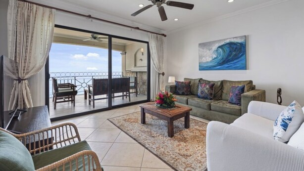 A spacious living area with a balcony, a ceiling fan, and a large painting of a wave. - Stunning Condo with Panoramic Beach, Ocean, and Mountain Views in Playa Flamingo (Playa Flamingo)