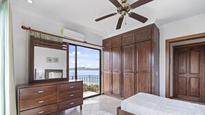 A bedroom with a large wooden wardrobe, a ceiling fan, and a view of the sea through a sliding door. - Stunning Condo with Panoramic Beach, Ocean, and Mountain Views in Playa Flamingo (Playa Flamingo)