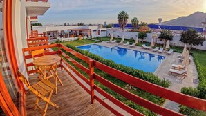 A balcony with a wooden floor, a pool, and lounge chairs. - Hotel La Colina Live the experience among dunes and nature (Cerro Prieto)