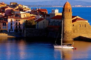 A coastal town with historic architecture, including a prominent tower and a white sailboat docked near the shore. - Apartment near the ocean with a private terrace and parking space - "Le Miramar" Residence (Argelès-sur-Mer)