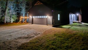 Un bâtiment à deux étages, doté d’un garage et d’une petite dépendance attenante, entouré d’arbres et bordé d’une allée en gravier.