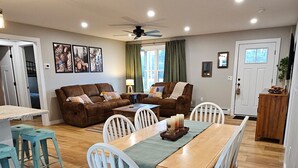 Un vaste espace de vie comprenant une table à manger, des chaises blanches, un canapé marron et un ventilateur de plafond.