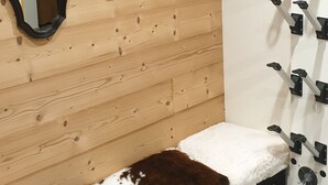 Ein Badezimmer mit Holzwand, einer Bank mit Kuhfellkissen, einem Spiegel und einem Handtuchhalter.