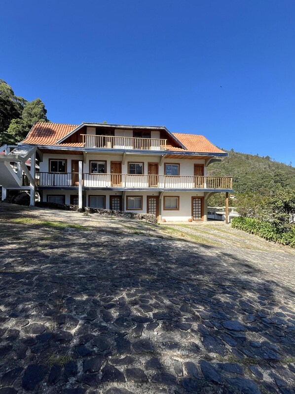 A two-story building with a tiled roof, multiple balconies, and a stone-paved entrance area.