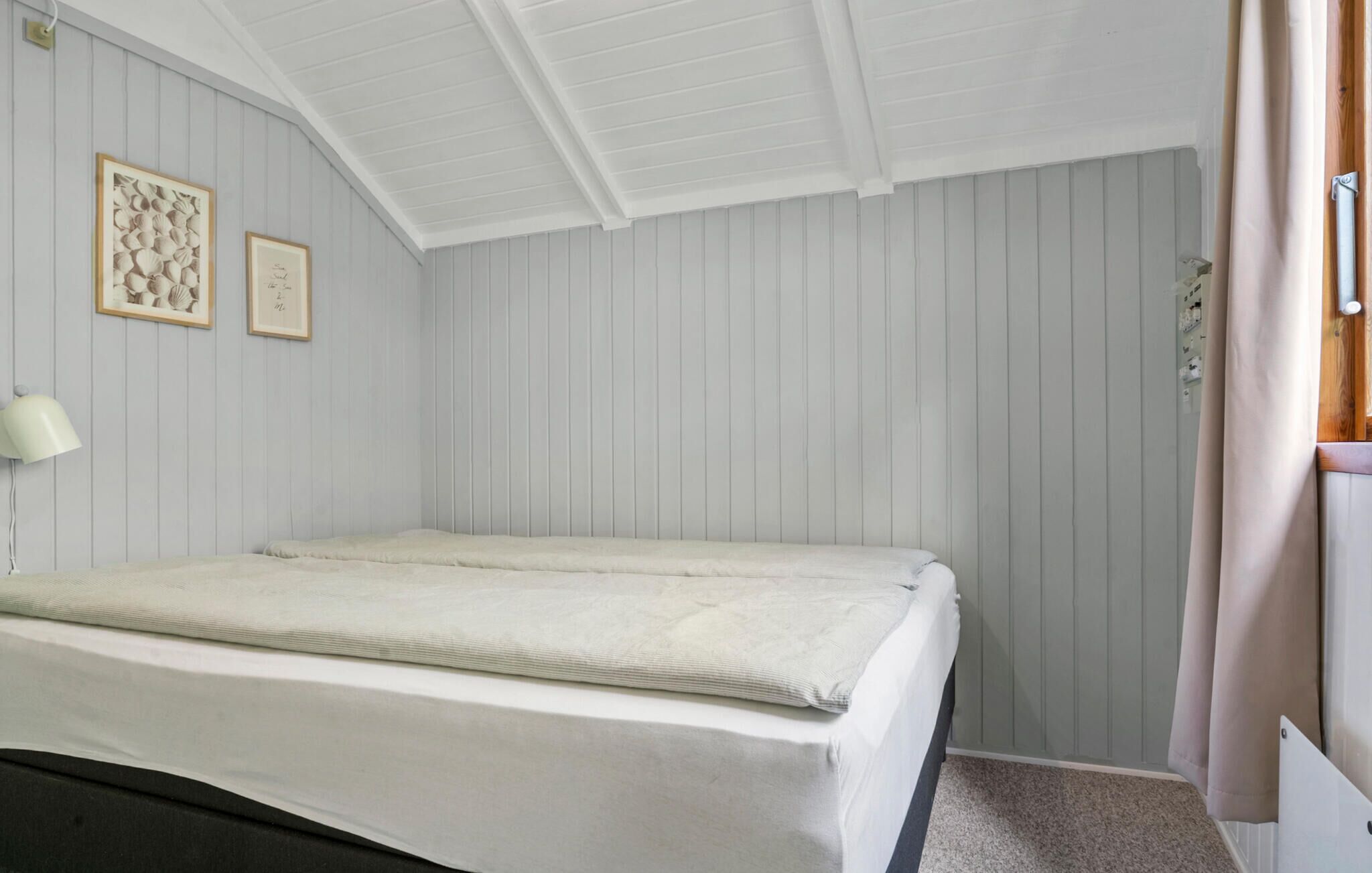 Une chambre à coucher avec un lit, une lampe et deux tableaux encadrés accrochés au mur.