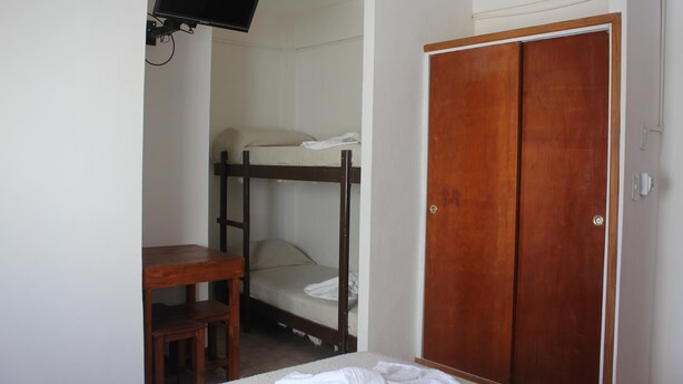 Una habitación con literas, un escritorio de madera, un televisor montado en la pared y un armario de madera.