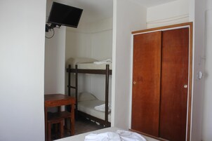 Una habitación con literas, un escritorio de madera, un televisor montado en la pared y un armario de madera.