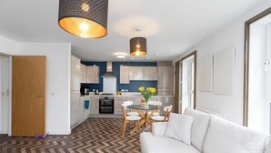 A modern kitchen with white cabinets, a dining table with chairs, and a white sofa in the living area.