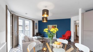 A modern living room with a glass dining table, white chairs, a sofa, and a red chair. There is a vase with yellow flowers on the table.
