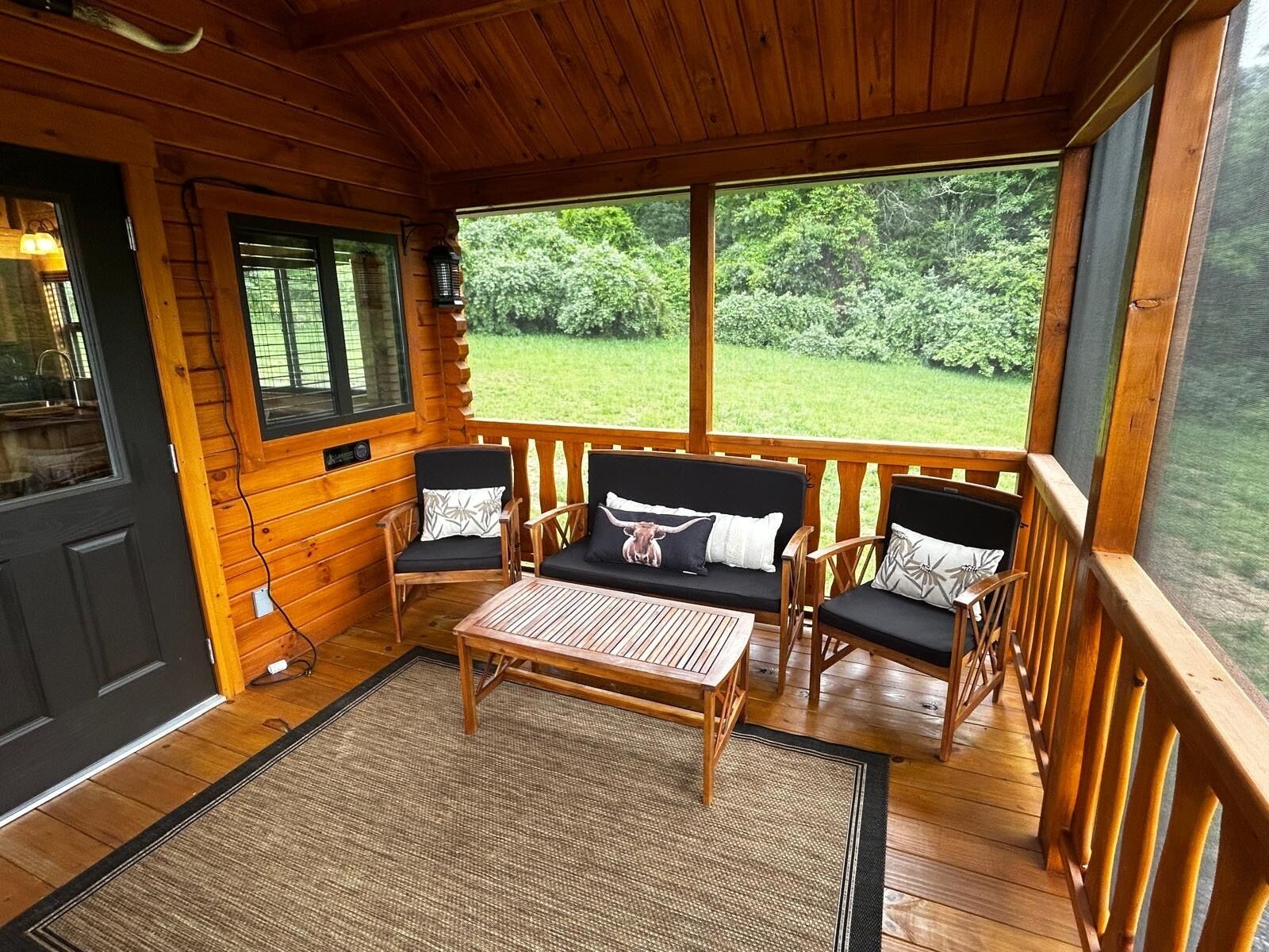 A wooden cabin with a porch, two chairs, a table, and a view of a green landscape.