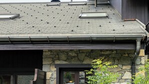 Uma casa com fachada de pedra, deck de madeira e telhado de metal com claraboias.