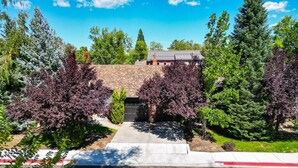 A residential property with a driveway leading to a garage, surrounded by mature trees and a clear blue sky. - Enchanting 2BR in Old Southwest (Reno)