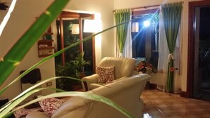 A living room with a beige sofa, a patterned pillow, a potted plant, and a view through a glass door. - Totem de Mar (Valeria del Mar)