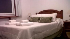 A neatly made bed with white linens and two pillows, a bedside table with a lamp, and a window with a view of the outside. - Totem de Mar (Valeria del Mar)