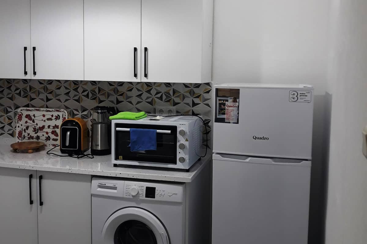 A compact kitchen with white cabinets, a washing machine, a microwave, a toaster, and a refrigerator.