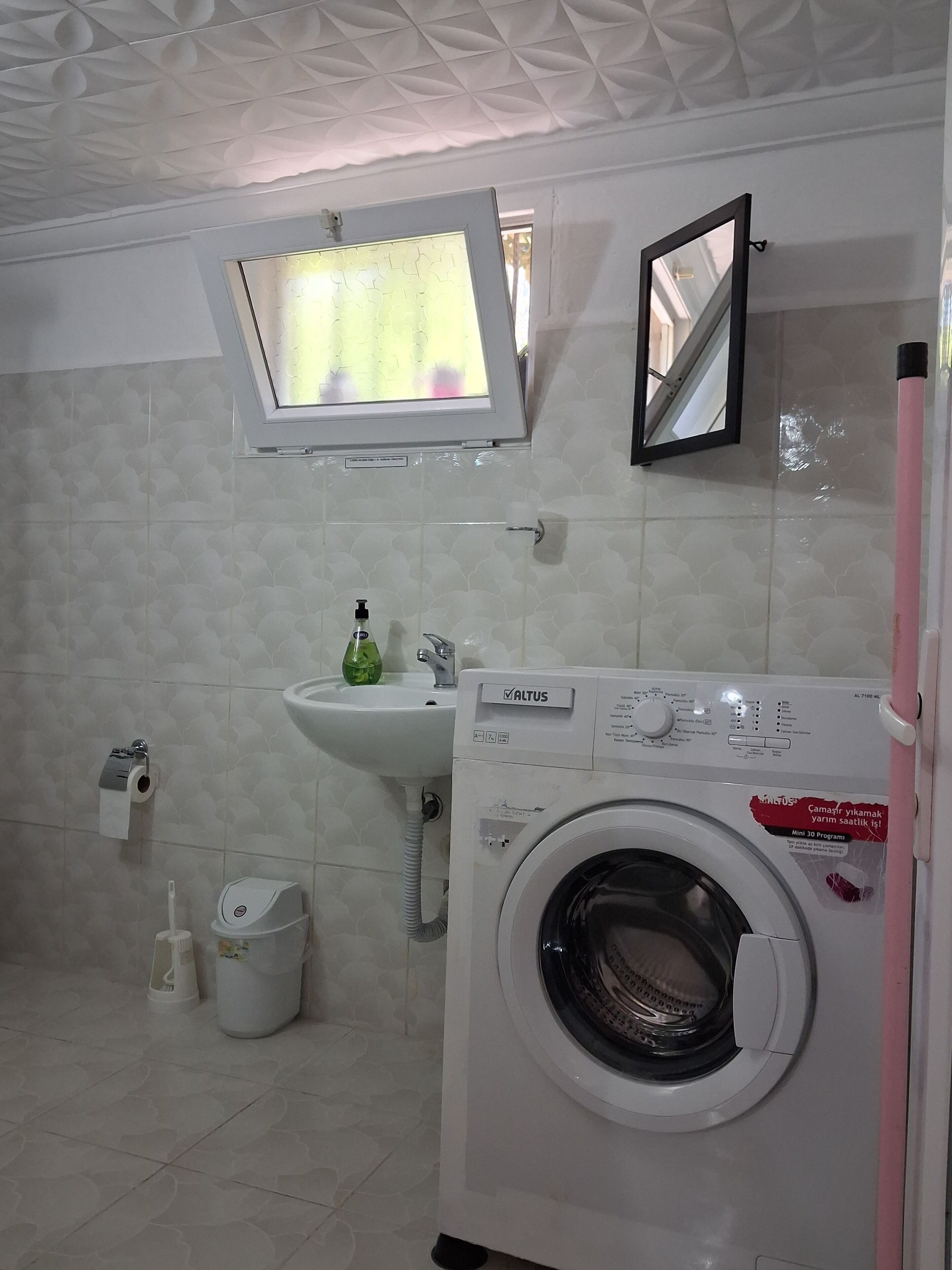Un baño pequeño con lavadora, lavamanos, espejo y soporte para papel higiénico.