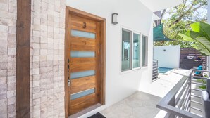 Een moderne entree met een houten deur, een glazen paneel en een klein balkon met een zwembad en buitenmeubilair.