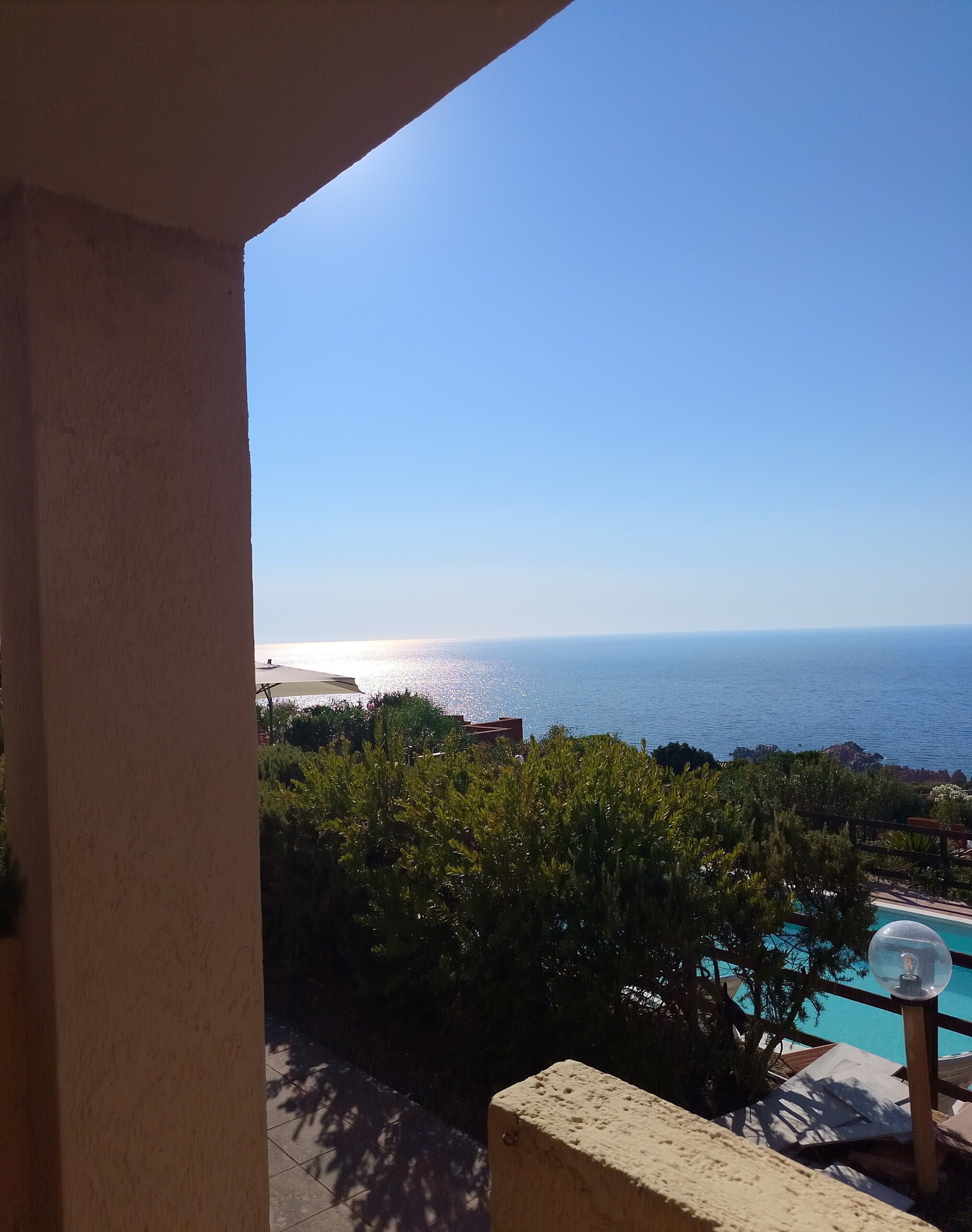 Un balcon avec vue sur la mer, une piscine et quelques plantes.