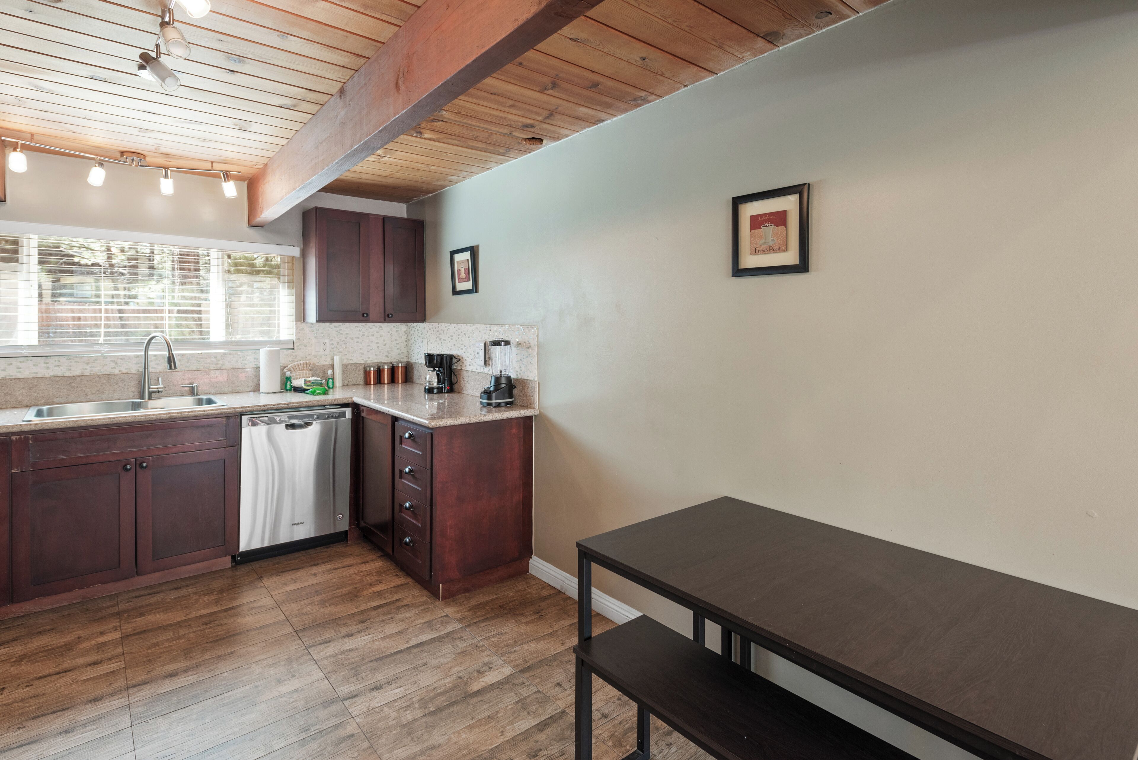 A kitchen with wooden cabinets, a dishwasher, a countertop with appliances, and a bench.