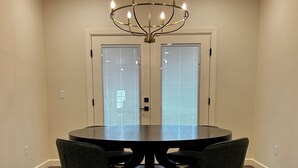 Un salón de conferencias con una mesa redonda, cuatro sillas, una araña y dos puertas con persianas.