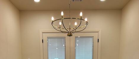 A conference room with a round table, four chairs, a chandelier, and two doors with blinds.
