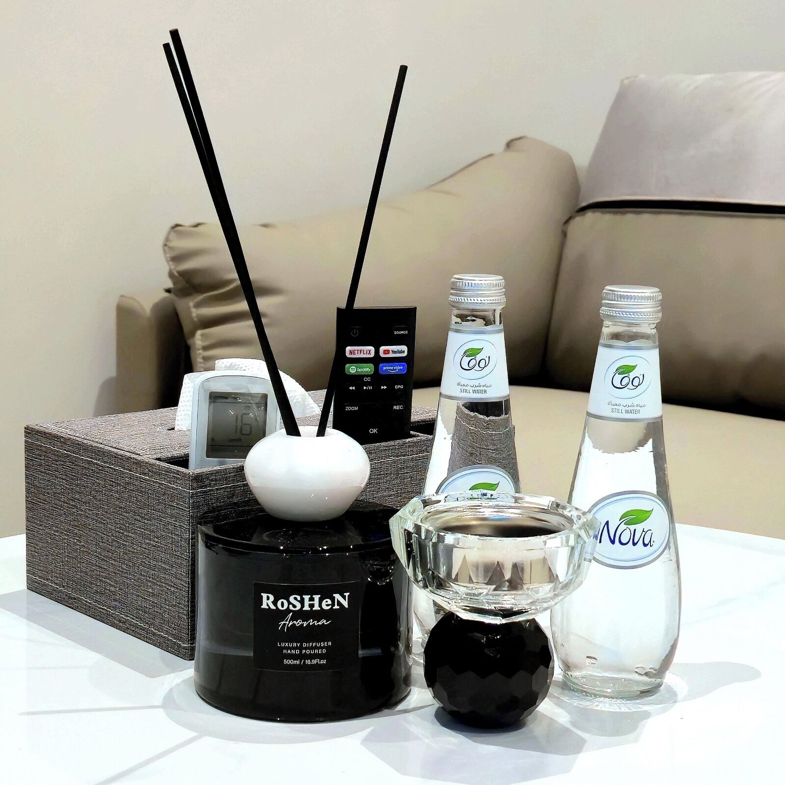 Una mesa con un difusor, dos botellas de agua, un control remoto y un reloj digital.