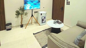 A modern living room with a flat-screen TV on a tripod, a small refrigerator, a coffee machine, a sofa, and a potted plant. -  فايان استديو مودرن بسرير مزدوج وصالة ودخول ذكي في المنطقة الحية في شمال بريدة (Buraydah)