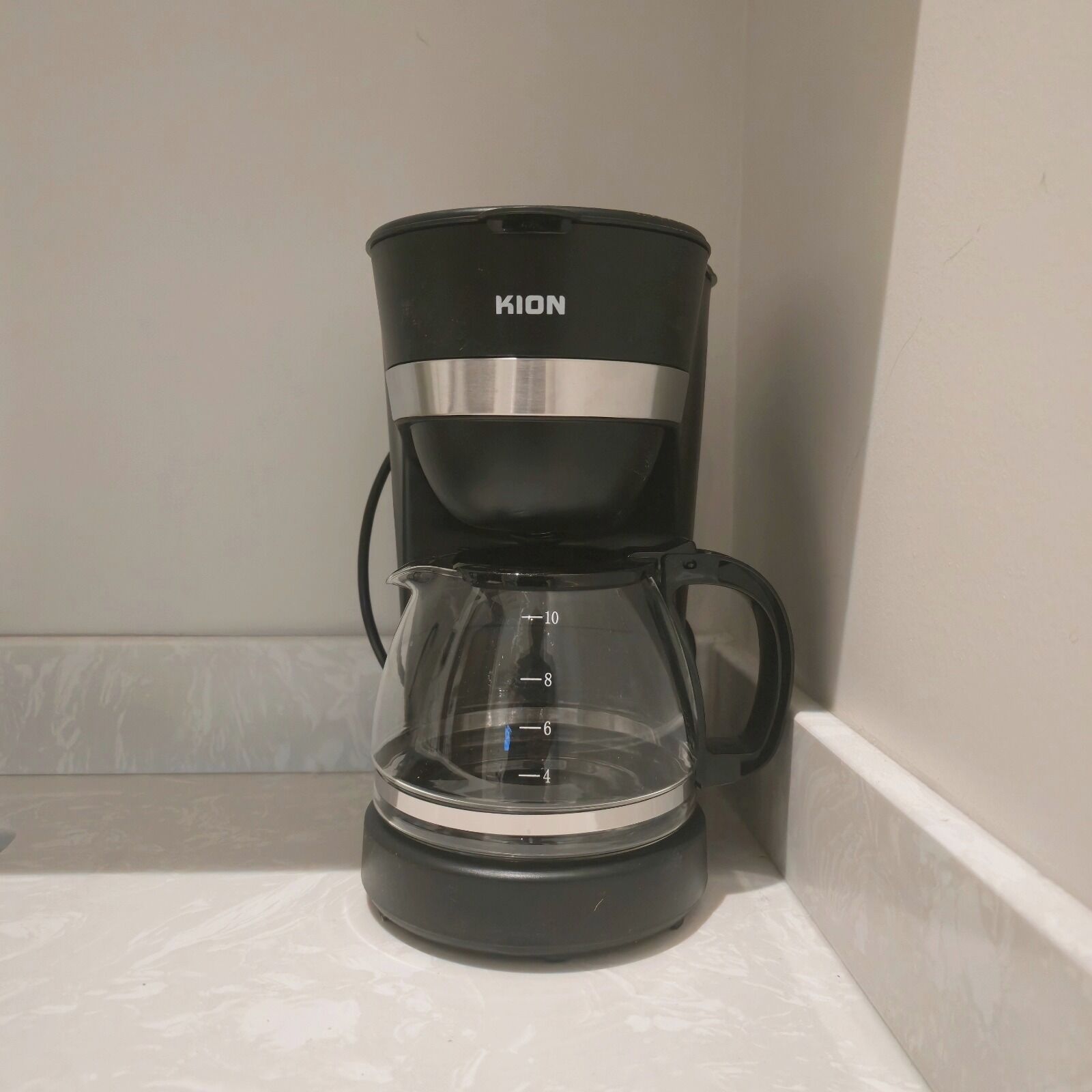 En svart KION-kaffebryggare med en genomskinlig kanna och måttmarkeringar, placerad på en vit bänkskiva.