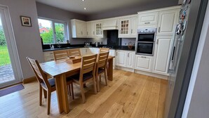 A modern kitchen with white cabinetry, a wooden dining table, and a skylight. - ☘️Spacious Family Home in Belfast (Belfast)