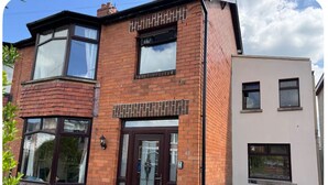 A two-story brick house with a dark brown front door, a small porch, and a garage door. - ☘️Spacious Family Home in Belfast (Belfast)