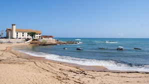 A beach with a building near the shore, boats in the water, and a clear sky. - Sopro de Iemanjá Hostal (Salvador)