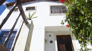 A white building with a wooden door, a window with metal bars, and a potted plant. - Sopro de Iemanjá Hostal (Salvador)