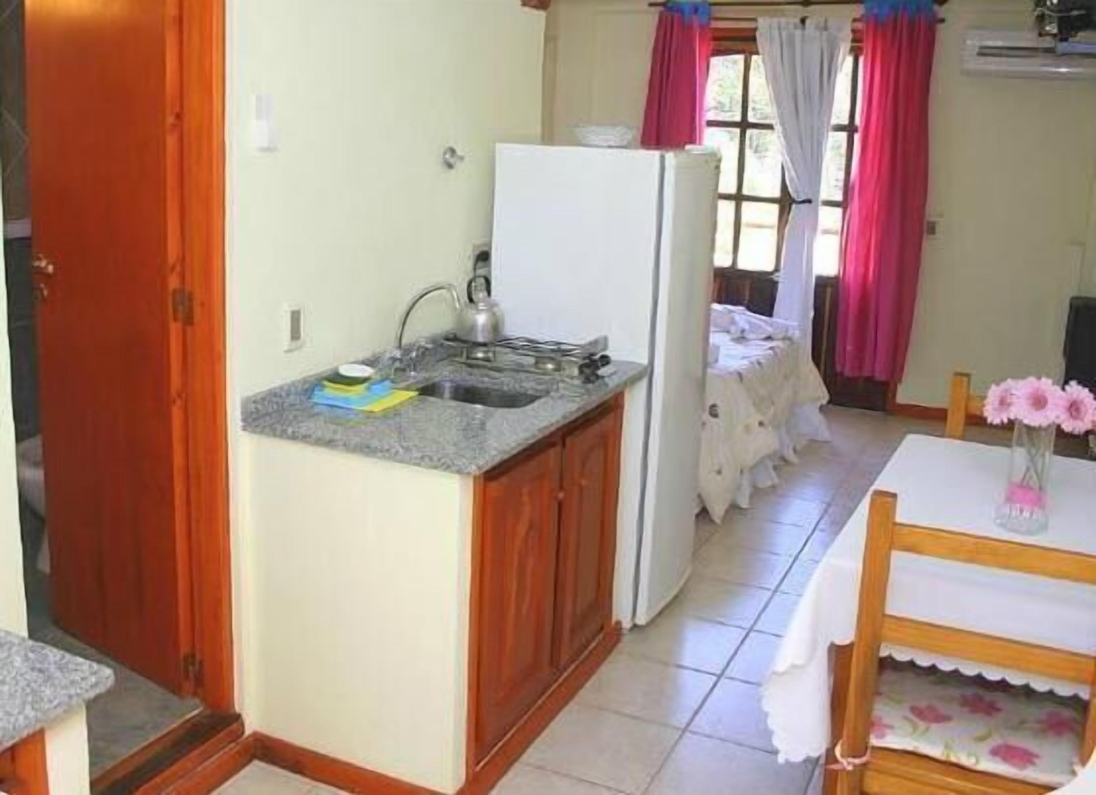 Een kleine keuken met een koelkast, gootsteen en een eethoek met een tafel en stoelen.