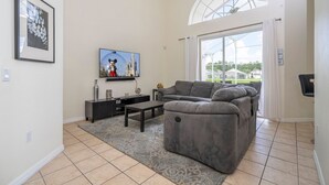 A living room with a gray sectional sofa, a flat-screen TV, a small coffee table, and a patterned rug. - Amazing 6 Bedrooms With Pool (Kissimmee)