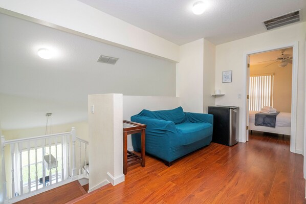 A living room with a wooden floor, a blue sofa, a small table, and a white railing. - Amazing 6 Bedrooms With Pool (Kissimmee)
