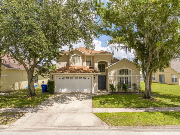 A two-story house with a garage, a covered front porch, and a well-maintained lawn. - Amazing 6 Bedrooms With Pool (Kissimmee)