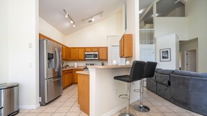 A modern kitchen with stainless steel appliances, wooden cabinets, and a bar stool. - Amazing 6 Bedrooms With Pool (Kissimmee)