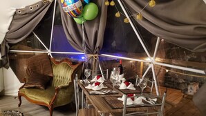 A tented dining area with a table set for two, a vintage armchair, and a view of the night sky. - The Glamp Inn (Lincolnton)