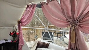 A cozy interior with a white sofa, pink curtains, and a wooden deck visible through the window. - The Glamp Inn (Lincolnton)