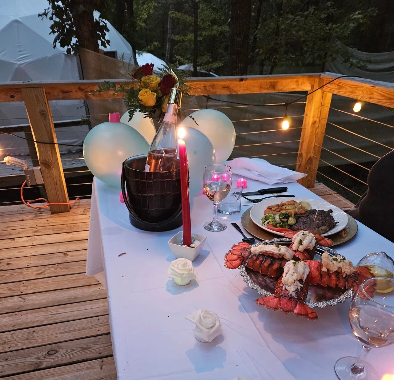 Mesa al aire libre con una vela, una botella y un plato de langosta.