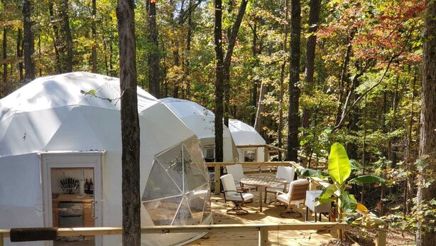 A dome-shaped tent with a wooden deck and seating area, surrounded by trees. - The Glamp Inn (Lincolnton)