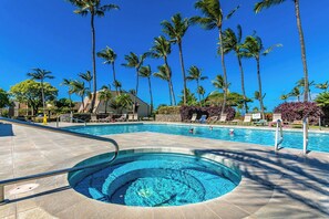 Une piscine avec un jacuzzi, entourée de palmiers et de chaises longues.